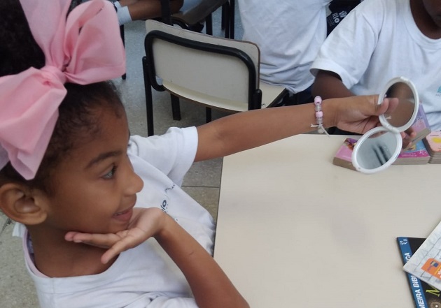 Menina negra com laço rosa no cabelo se olha no espelho